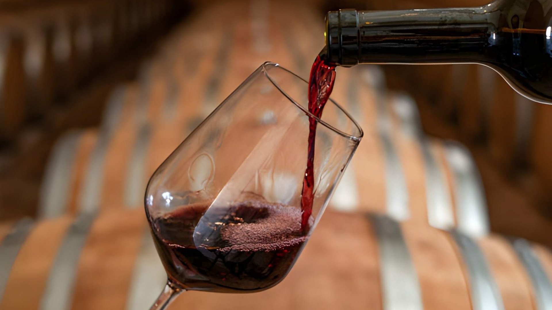 Fine red wine pouring into crystal glass in authentic oak barrel cellar